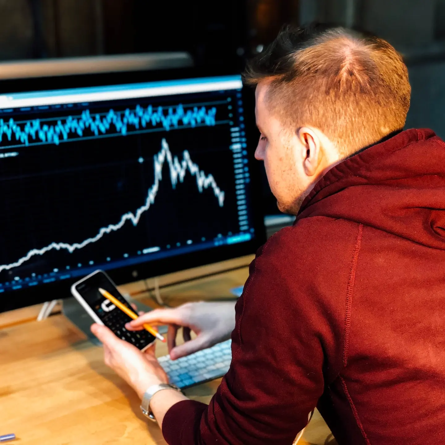 man holding black smartphone with flat screen monitor in front